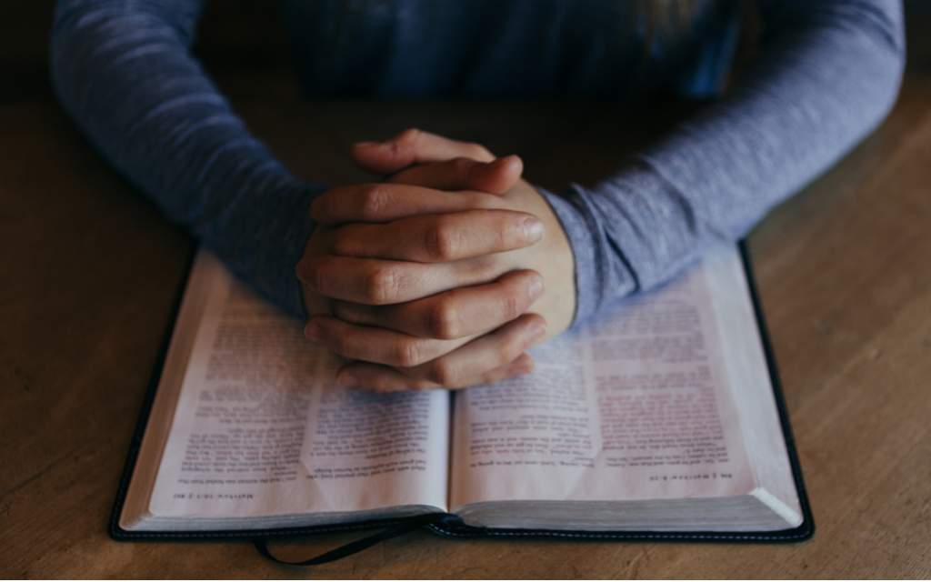 two hands clasped on an open Bible, how to pray