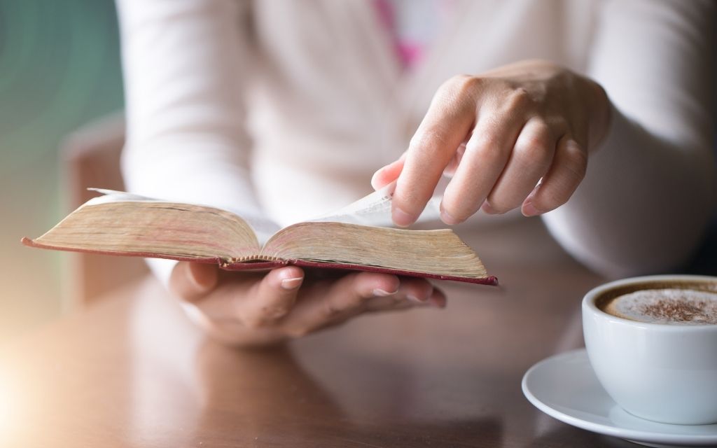 A lady reading a Bible with a cup of coffee